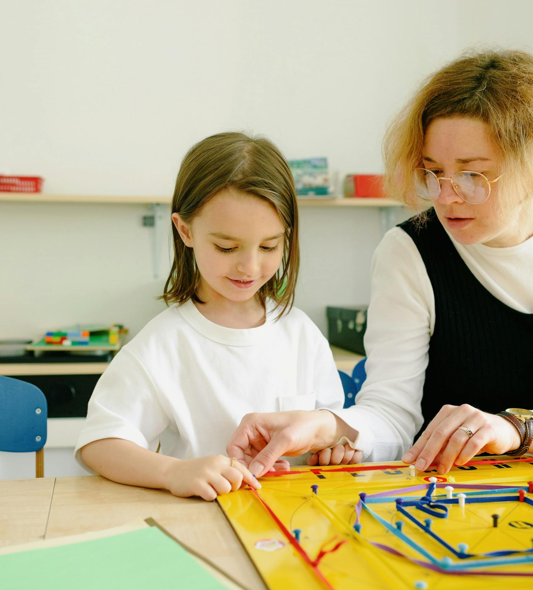 Adult gives child consultation as student works on yellow circuit board at classroom table.